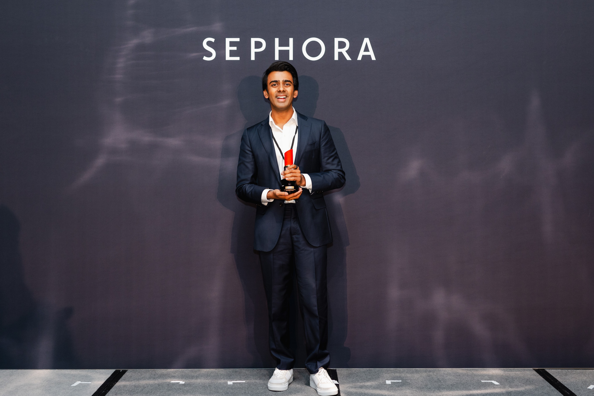 A man in a dark suit holding an award stands in front of a Sephora backdrop, exemplifying top-notch corporate photography.