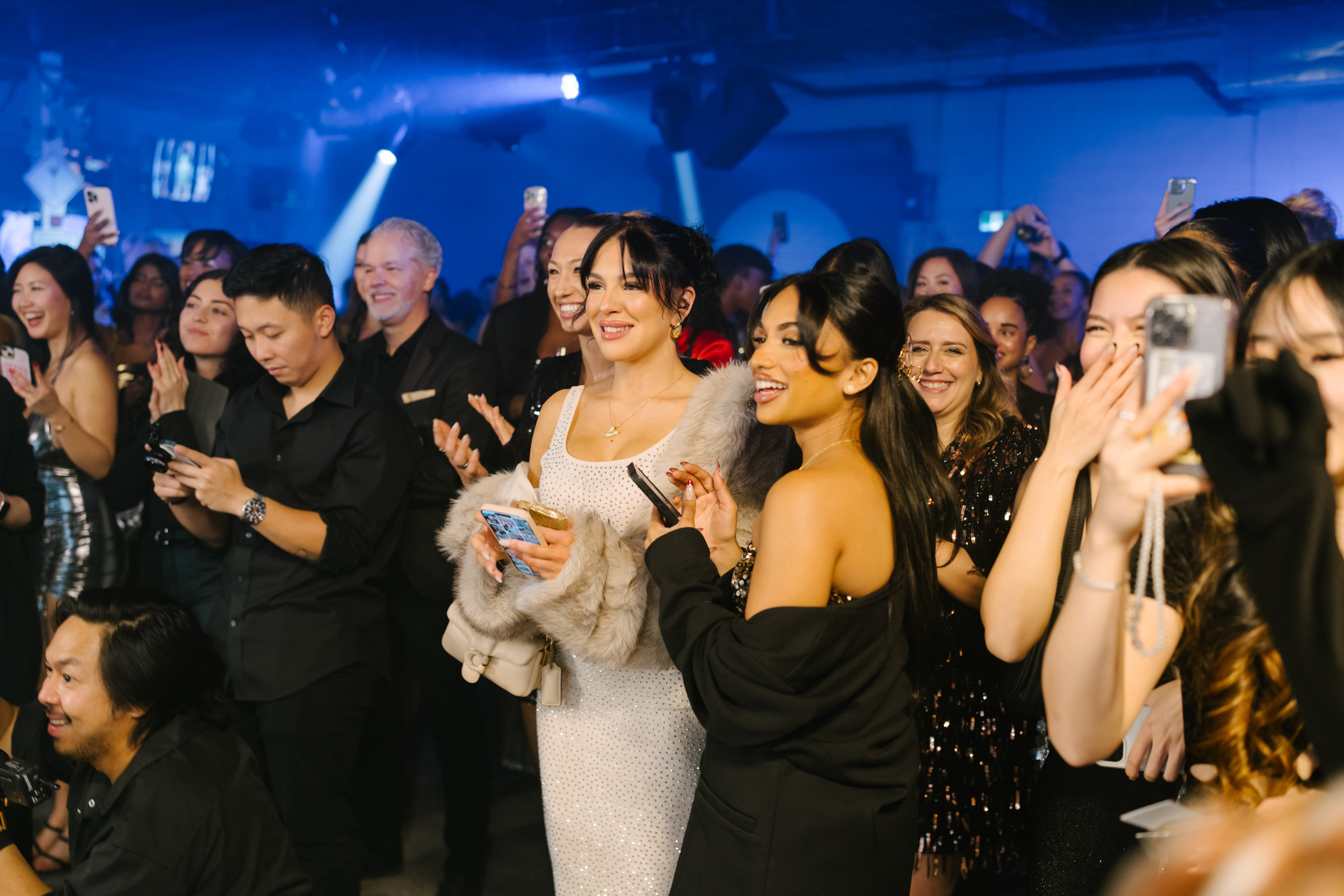 A large group of people at an indoor event, smiling and taking photos with their smartphones, capturing moments perfect for corporate photography.
